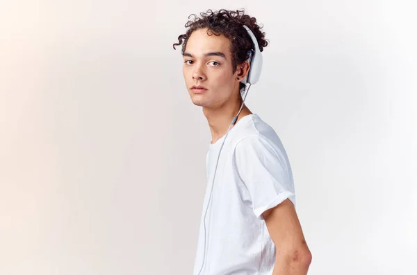 Έφηβος αγόρι σε ένα t-shirt ακούγοντας μουσική σε ακουστικά σε ένα ελαφρύ φόντο περικοπεί προβολή γκρο πλαν — Φωτογραφία Αρχείου