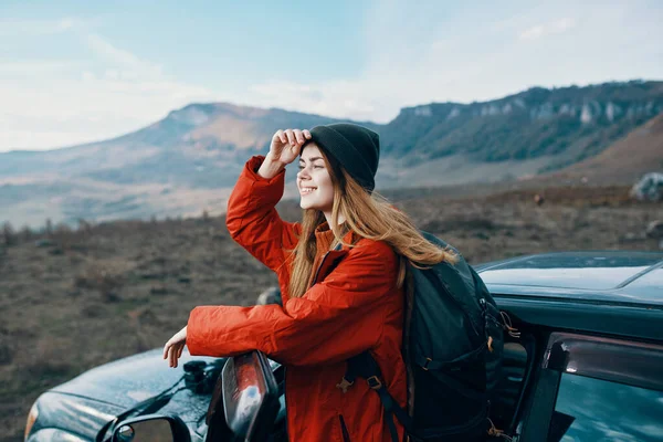 Mujer en un sombrero con una mochila en la espalda apoyada en la puerta de un coche en las montañas al aire libre — Foto de Stock