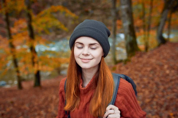 Glückliche Frau mit Rucksack reist im Herbst durch den Park und gestikuliert mit den Händen des Flusses im Hintergrund — Stockfoto