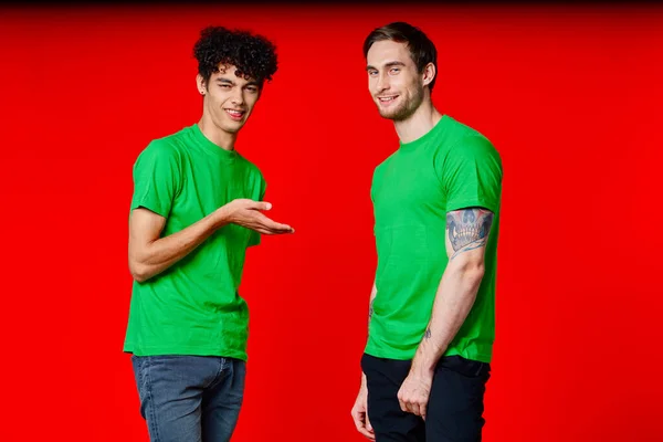 Zwei Freunde in grünen T-Shirts Spaß Kommunikation roter Hintergrund — Stockfoto