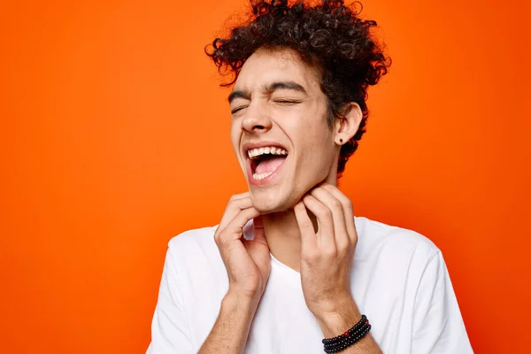 Carino ragazzo in bianco t-shirt e divertimento emozioni close-up arancione sfondo — Foto Stock