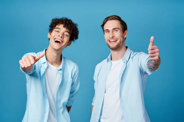 Два друга в одинаковых футболках и футболке, жестикулирующие руками на синем фоне — стоковое фото