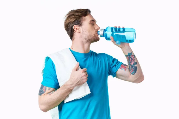 Man athlete drinks water from a bottle on a white background and a towel on his shoulder — Stock Photo, Image