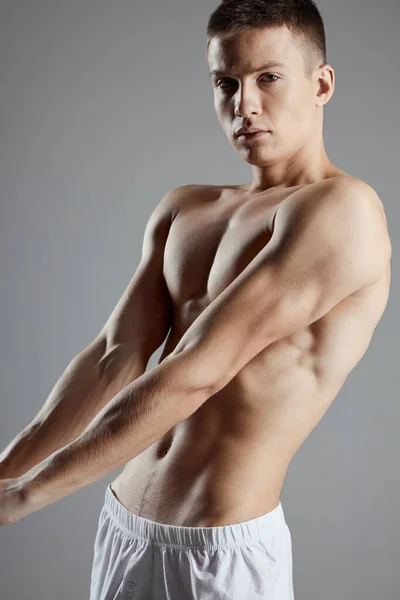 Man bodybuilder in witte shorts gebaren met handen op grijze achtergrond — Stockfoto