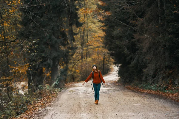 Viagem feliz com uma mochila em uma camisola quente, calças e botas caminha ao longo da estrada na floresta de outono — Fotografia de Stock
