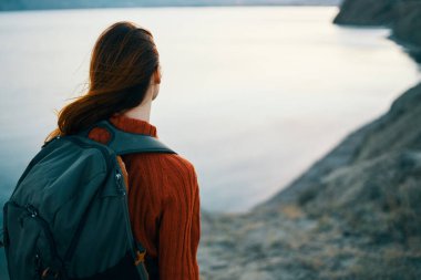 Sırt çantalı, turistik deniz dağları manzaralı kırmızı kazaklı kadın.
