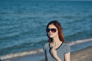 Kadın tişörtü sahilde, dağlarda deniz manzarası yakınında.