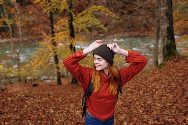 Woman tourist in a sweater hat with a backpack near tall trees in autumn in the forest — Stock Photo, Image