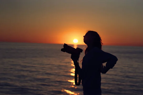 一名妇女的肖像，日落时分，她带着相机出现在海滩上 — 图库照片