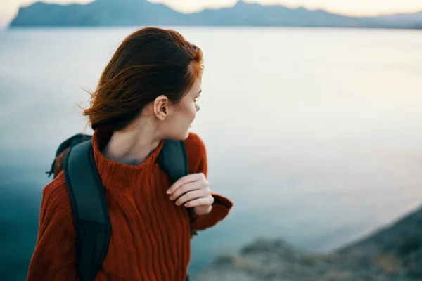 Donna in un maglione vicino al mare in montagna guarda di lato e uno zaino sulla schiena — Foto Stock