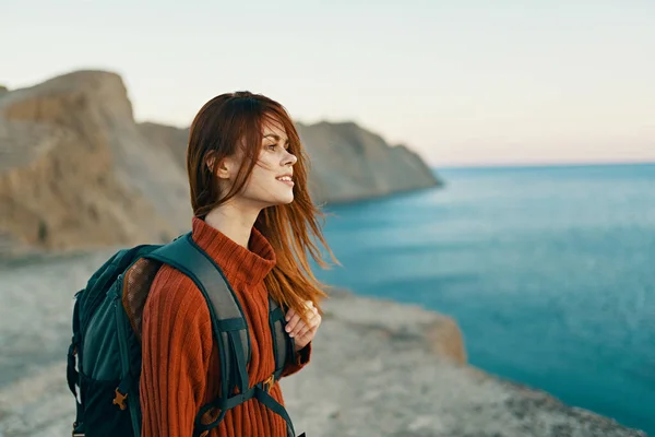 Гарна жінка у зв'язку з рюкзаком на спині в горах біля моря модель вигляду збоку — стокове фото