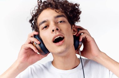 Kulaklıklı kıvırcık saçlı adam hafif bir arka planda müzik dinliyor.