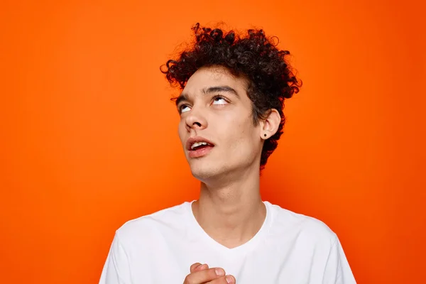 Joven chico en blanco camiseta rizado pelo sonrisa naranja fondo — Foto de Stock