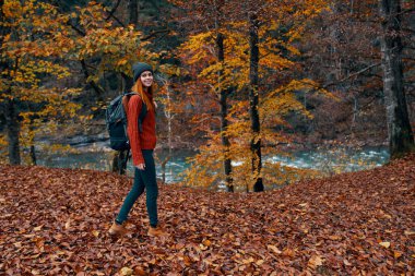 Sırt çantalı bir gezgin sonbaharda nehrin yanındaki parkta yürür.