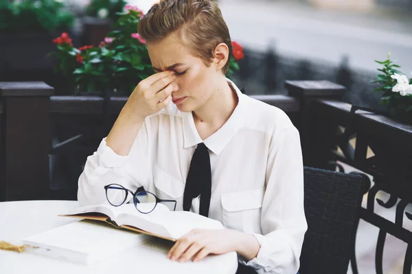 Femme lisant un livre à une table dans un restaurant éducation émotions lunettes fleurs en arrière-plan — Photo