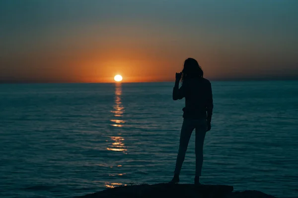 Η σιλουέτα μιας γυναίκας στο ηλιοβασίλεμα κοντά στη θάλασσα με τα χέρια προς τα πίσω — Φωτογραφία Αρχείου