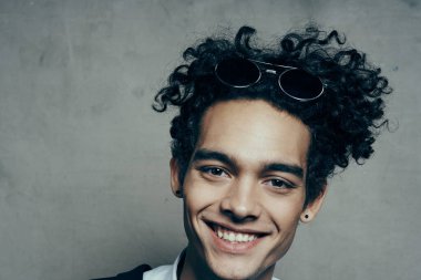 Beyaz gömlekli ve ceketli kıvırcık saçlı yakışıklı adam. Arka planda gri bir fotoğrafçılık stüdyosu portresi.