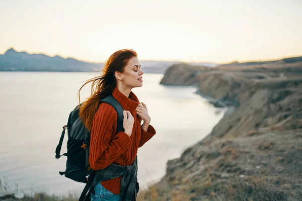 Жінка туристка в светрі з рюкзаком в горах біля моря вид збоку — стокове фото