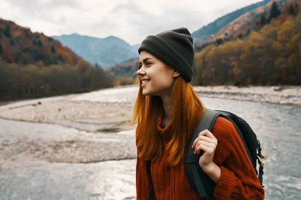 Ευτυχισμένος ταξιδιώτης με ένα σακίδιο σε ένα καπέλο και ένα πουλόβερ στα βουνά κοντά στο ποτάμι — Φωτογραφία Αρχείου