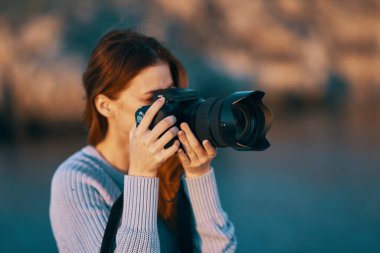 Kadın, doğada ve denizde objektifle kamerayı tutuyor. 