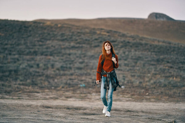 woman traveler in a red jeans sweater with a backpack on her back in the mountains