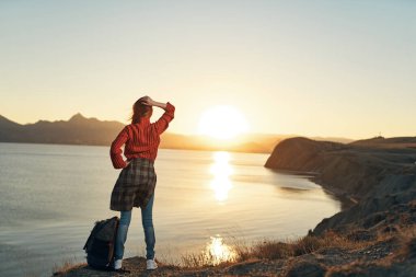 Elleri havada neşeli bir kadın gün batımına bakıyor. Seyahat özgürlüğü.