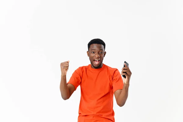 Homem emocional em uma camiseta laranja com um telefone em suas mãos alegria estúdio — Fotografia de Stock