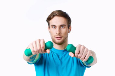 Elinde dambıllar olan mavi tişört egzersiz kulaklıkları olan bir adam.