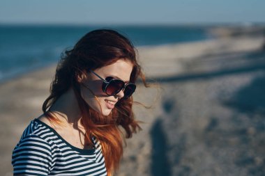 Gün batımında ya da balkondan deniz manzaralı yerde gözlüklü ve çizgili tişörtlü bir kadın.