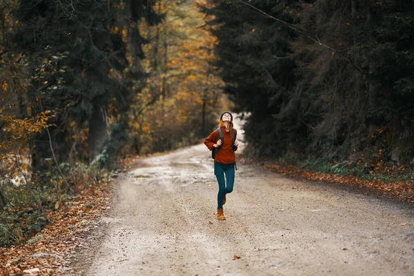 Donna energica che corre lungo la strada con lo zaino nella foresta autunnale — Foto Stock