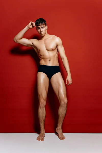 Atletik fiziği olan, siyah külotlu, kırmızı arka planda büyüyen seksi bir adam. — Stok fotoğraf