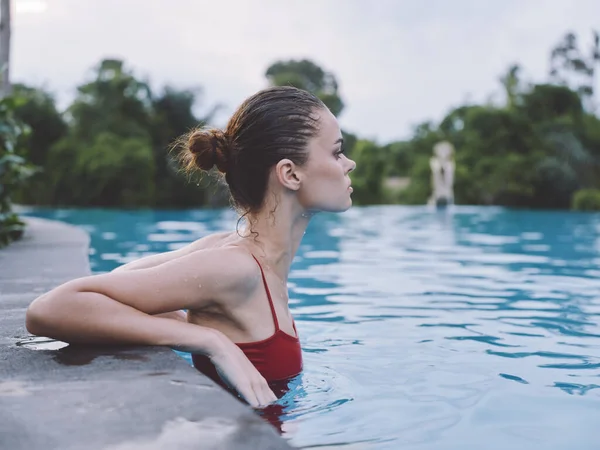 Uma mulher de fato de banho está inclinada sobre os azulejos da piscina e fica em vista lateral transparente da água — Fotografia de Stock