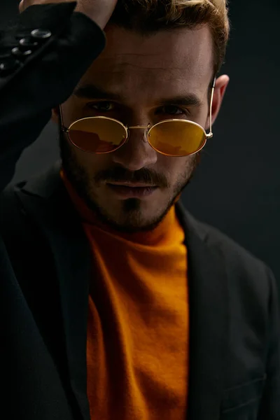 Um cara brutal com óculos e uma jaqueta preta camisola laranja fundo escuro — Fotografia de Stock