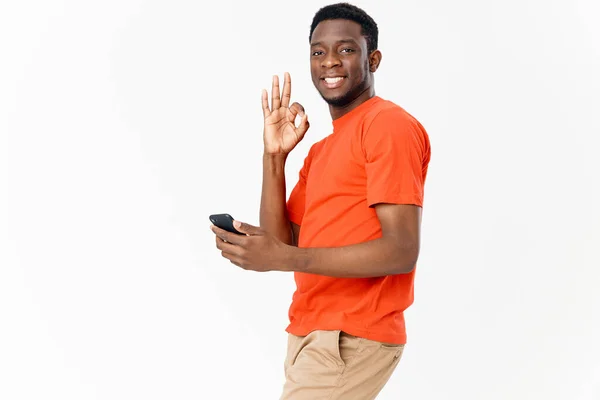 Heureux gars d'apparence africaine gesticulant avec ses mains et tenant un téléphone mobile — Photo