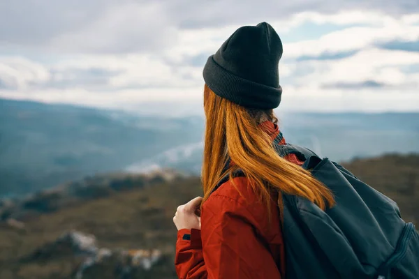 Γυναίκα σε ένα καπέλο σακάκι και ένα σακίδιο κοιτάζει τα βουνά στην απόσταση στη φύση — Φωτογραφία Αρχείου