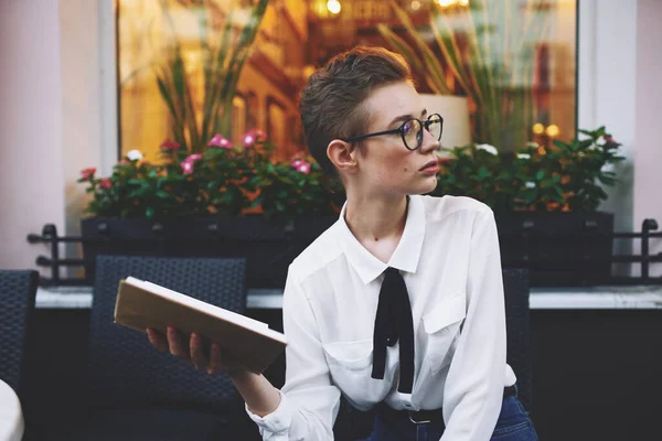 Красивая молодая женщина с короткими волосами в очках с книгой в руках за столом в кафе — стоковое фото