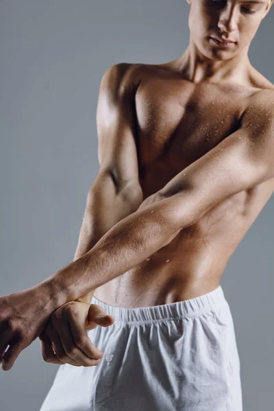 Atleta em shorts brancos em um fundo cinza gestos com as mãos fisiculturista fitness — Fotografia de Stock