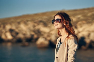 Yazın dağlarda güneş gözlüğü takan kızıl saçlı bir kadının portresi.