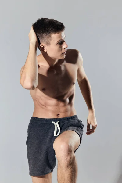Uomo sportivo in pantaloncini facendo esercizio appoggiato in avanti su sfondo grigio vista ritagliata — Foto Stock