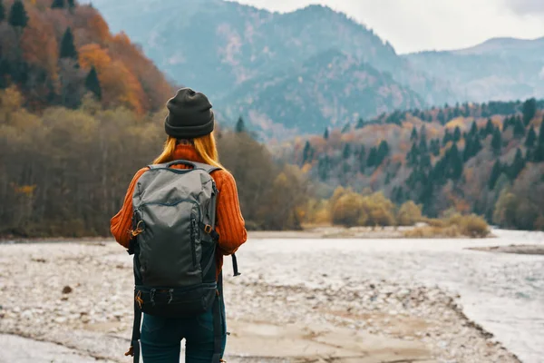 Woman travels in the mountains in autumn near the river in nature with a backpack back view — Stock Photo, Image