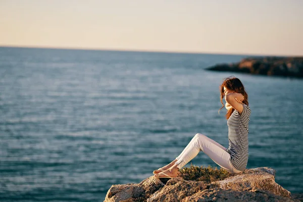 Woman by the sea sits on a large stone side view — Stock Photo, Image