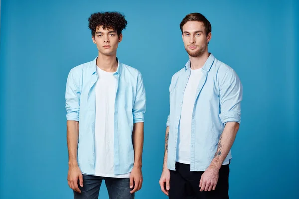 Riccio ragazzo in una camicia si trova accanto a un giovane uomo in una t-shirt su uno sfondo blu vista ritagliata — Foto Stock