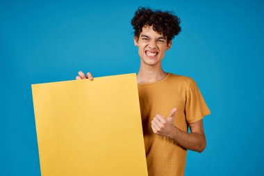 Kıvırcık saçlı, neşeli adam sarı poster modeli, mavi arka plan.