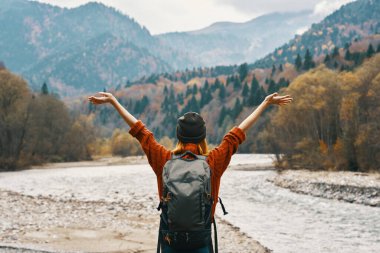 Dağlarda mutlu bir kadın doğada nehrin kenarında gezer ve ellerini kaldırır.