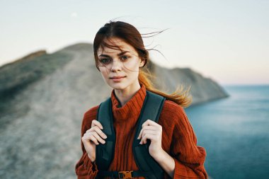 Doğa dağları temiz hava ve sırt çantası ve süveteri olan genç bir gezgin deniz kenarında dinleniyor.