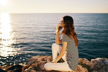 Tişörtlü ve pantolonlu bir kadın deniz günbatımı güneşinin portresini yapıyor.