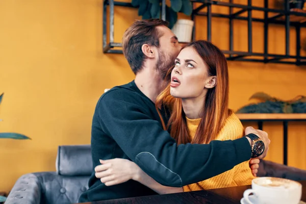 Jovens apaixonados abraçando enquanto sentados em uma mesa em um café e parede interior laranja — Fotografia de Stock