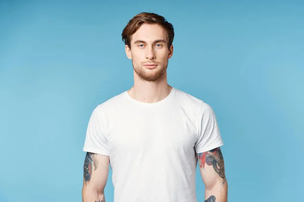 Kollarında dövmesi olan bir adam beyaz tişört kırpılmış mavi arka plan. — Stok fotoğraf