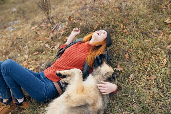 Kobieta turysta leżący na trawie obok pies przyjaźń zabawy gry — Zdjęcie stockowe