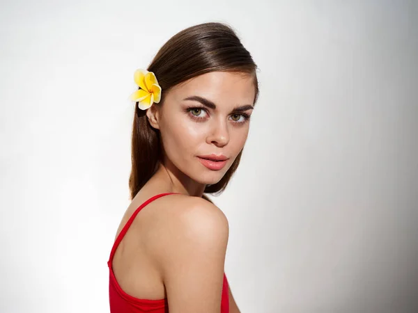 Modelo atraente em t-shirt vermelha e flor no cabelo mulher luz fundo — Fotografia de Stock